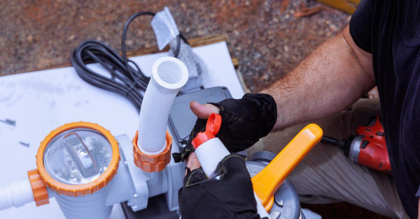 Close-up to the hands of a man wearing black gloves putting together a white filtration system with orange details.