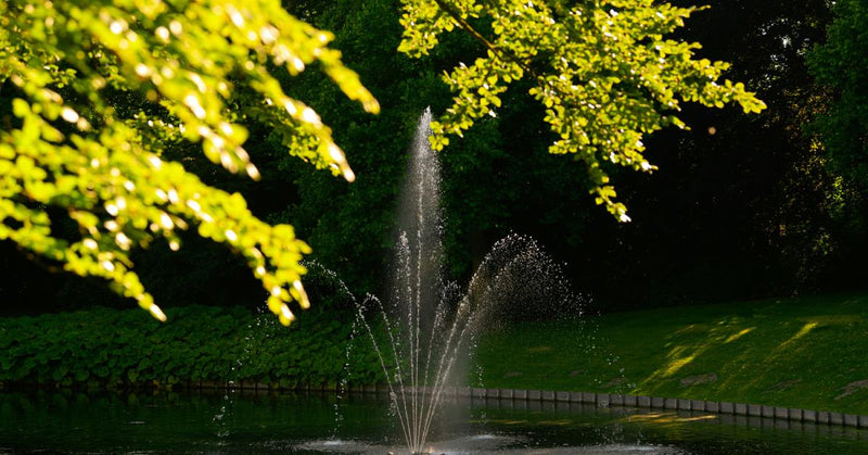 A round pond surrounded by rectangular bricks at the border. A center fountain sprays water up in several arches.
